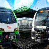 Zwei moderne Züge, ein grüner DB und ein weißer RRX, stehen nebeneinander am Bahnsteig.