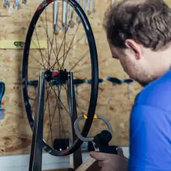 Mann zentriert Laufrad mit Messwerkzeug. Werkzeuge hängen an der Wand.