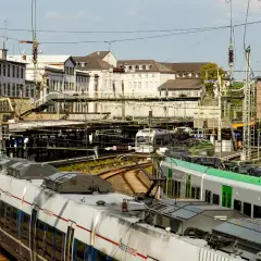 Zwei Züge stehen auf Gleisen vor Gebäuden. Ein Zug ist weiß mit roten Streifen, der andere grün. Perfekt für das db semesterticket nrw.