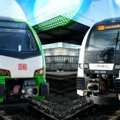 Zwei moderne Züge, ein grüner DB und ein weißer RRX, stehen nebeneinander am Bahnsteig.