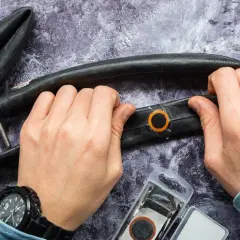 Hände reparieren einen Fahrradschlauch mit einem Flicken. Werkzeug und Flickzeug liegen bereit.
