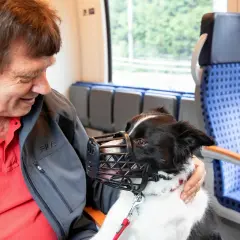 Ein Mann mit seinem Hund im Zug in NRW. Der Hund trägt einen Maulkorb und schaut freundlich.