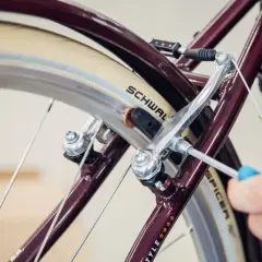 Hand wechselt Bremsbacken am Fahrrad mit Schraubendreher. Nahaufnahme des Bremsmechanismus am Rad.