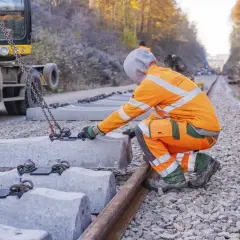 Arbeiter bei Bauarbeiten der Deutschen Bahn in NRW legen neue Betonschwellen. Ein Bagger hebt die schweren Teile an.