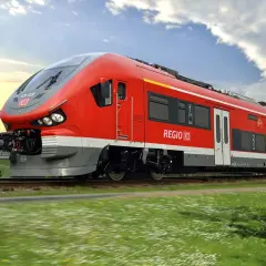 Roter Pesa-Zug der Deutschen Bahn fährt durch eine grüne Landschaft unter blauem Himmel.
