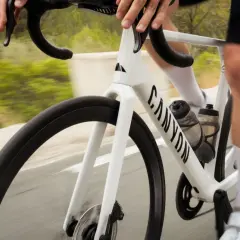 Ein weißes Rennrad in voller Geschwindigkeit auf einer Straße, die Landschaft verschwimmt. Der Fahrer hält die Lenker fest, die Beine treten kräftig in die Pedale.