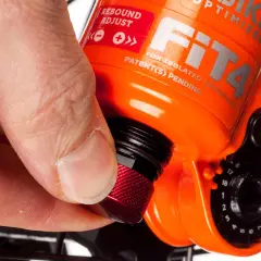 Hand dreht roten Knopf zur Federgabel einstellen. Rebound Adjust ist auf der orangefarbenen Gabel sichtbar.