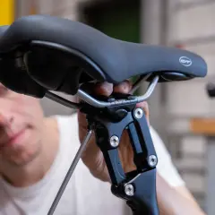 Mann stellt Fahrradsattel ein. Mit Inbusschlüssel wird die Sattelstütze justiert, um den Fahrradsattel wechseln zu können.