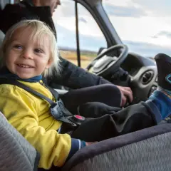 Glückliches Kind im Kindersitz im Bus. Die Füße des Kindes ragen über das Armaturenbrett.