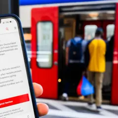 Smartphone zeigt Deutschland-Ticket mit Vorteilen: unbegrenzt reisen, deutschlandweit gültig, 58 Euro/Monat. Bahnsteig mit einsteigenden Reisenden im Hintergrund.