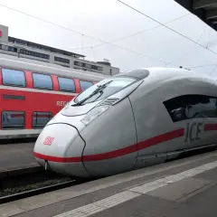 ICE-Zug und roter Regionalzug am Bahnsteig. Der ICE ist bereit für die Fahrt, wie ein ausgedrucktes Ticket zum Einsteigen.