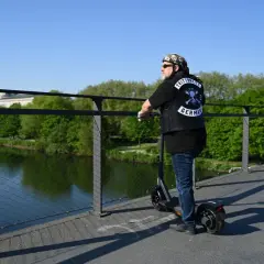 Mann mit Weste und Totenkopf-Bandana auf E-Scooter, genießt die Aussicht. Die Reichweite des E-Scooters ist für die Fahrt über die Brücke ausreichend.
