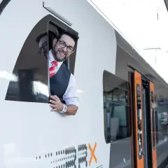 Ein freundlicher Lokführer winkt aus dem Fenster eines RRX Zuges.