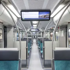 Innenraum eines modernen Zuges mit blauen Sitzen und einem Bildschirm, der die S-Bahn Köln zeigt. Die et 424 ist bereit für die nächste Fahrt.