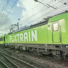 Ein grüner FlixTrain fährt auf Gleisen, im Hintergrund ist eine Kathedrale zu sehen. Perfekt für eine Reise mit dem Deutschlandticket.