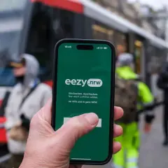 Hand hält Smartphone mit eezy.nrw App. Einfach einchecken, auschecken und nur nach Luftlinie zahlen in Westfalen.