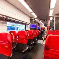Rote Sitze im modernen Desiro ML Zug der ÖBB. Die Sitze sind mit dem ÖBB-Logo versehen und laden zu einer angenehmen Reise ein.