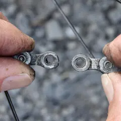 Hände halten die beiden Enden einer gerissenen Fahrradkette auseinander.
