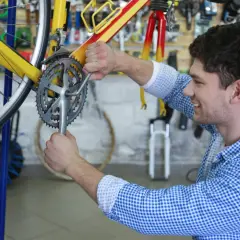 Ein Mann restauriert ein gelbes Fahrrad in einer Werkstatt. Er schraubt mit einem Werkzeug an der Kurbel.