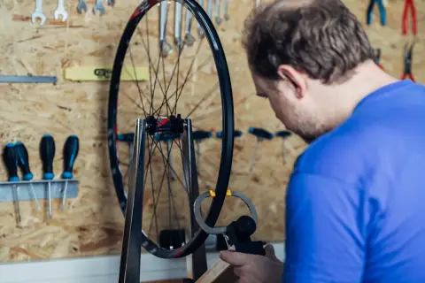 Mann zentriert Laufrad mit Messwerkzeug. Werkzeuge hängen an der Wand.