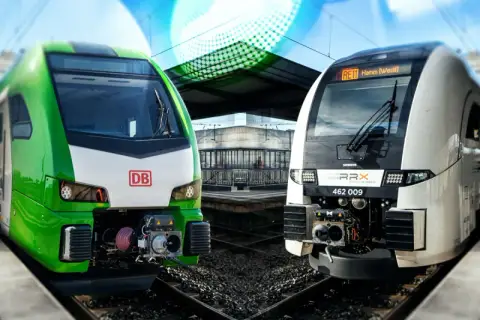 Zwei moderne Züge, ein grüner DB und ein weißer RRX, stehen nebeneinander am Bahnsteig.