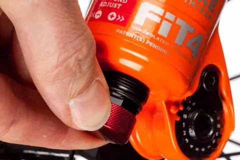 Hand dreht roten Knopf zur Federgabel einstellen. Rebound Adjust ist auf der orangefarbenen Gabel sichtbar.
