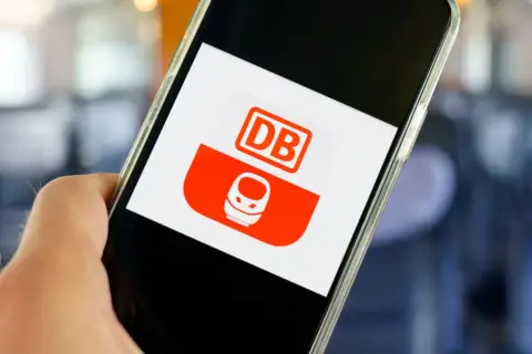 Hand hält Smartphone mit DB-App. Hier kann man unkompliziert ein DB Ticket stornieren.