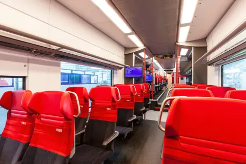 Rote Sitze im modernen Desiro ML Zug der ÖBB. Die Sitze sind mit dem ÖBB-Logo versehen und laden zu einer angenehmen Reise ein.