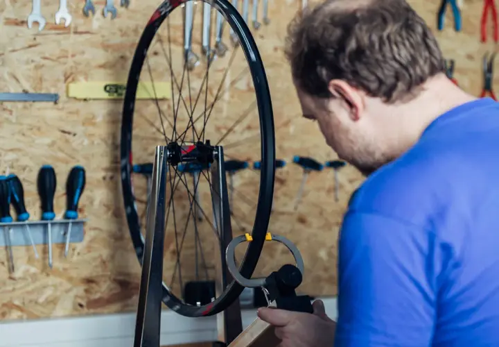 Mann zentriert Laufrad mit Messwerkzeug. Werkzeuge hängen an der Wand.