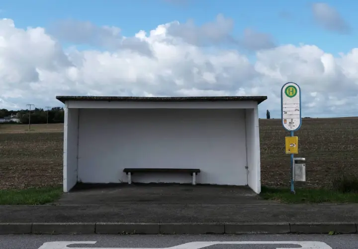 Ein Bushäuschen mit Bank und Haltestellenschild. Dieses Verkehrsmittel mit H-Symbol wartet auf Fahrgäste.