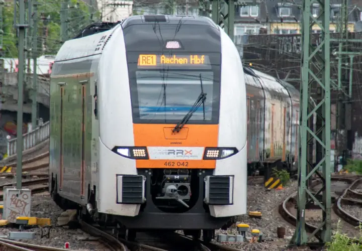 Ein moderner Zug der SPNV Linien NRW fährt auf Gleisen. Die Anzeige zeigt "RE1 Aachen Hbf".