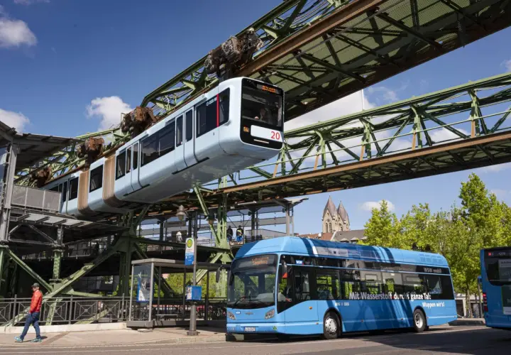 Die Schwebebahn Wuppertal fährt über einem blauen Bus. Mit dem Deutschlandticket ist das ganze Tal mobil.