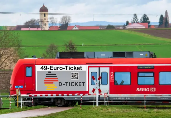 Rote Bahn mit "49-Euro-Ticket" Aufdruck fährt durch ländliche Gegend. Das rrx deutschlandticket macht Reisen günstig.