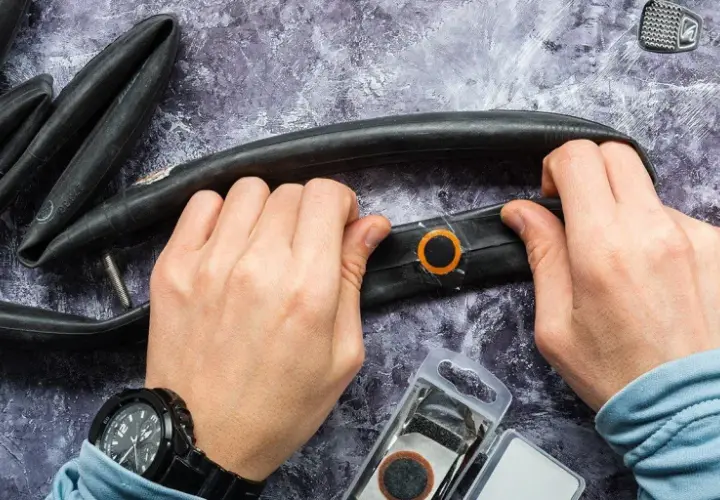 Hände reparieren einen Fahrradschlauch mit einem Flicken. Werkzeug und Flickzeug liegen bereit.