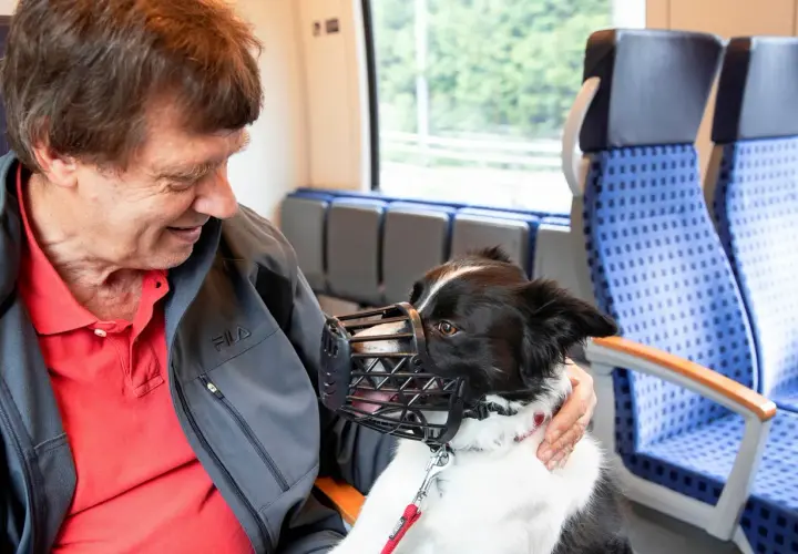 Ein Mann mit seinem Hund im Zug in NRW. Der Hund trägt einen Maulkorb und schaut freundlich.