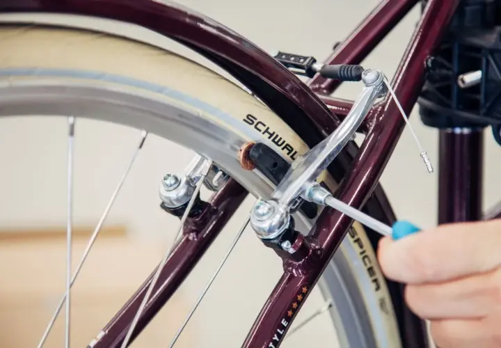 Hand wechselt Bremsbacken am Fahrrad mit Schraubendreher. Nahaufnahme des Bremsmechanismus am Rad.