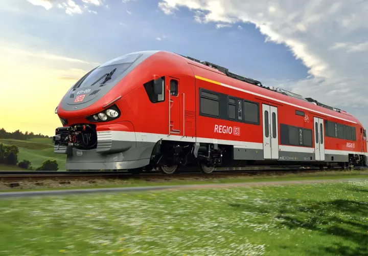 Roter Pesa-Zug der Deutschen Bahn fährt durch eine grüne Landschaft unter blauem Himmel.