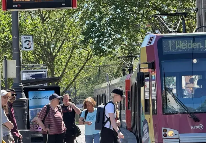 Menschen warten an Gleis 3 auf die Bahn. Die Anzeige zeigt "1 Weiden", was die einfache Fahrt Bedeutung für die Reisenden verdeutlicht.
