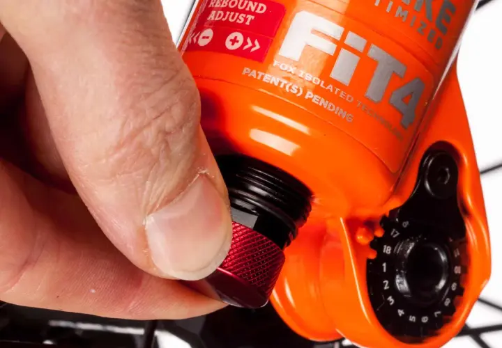 Hand dreht roten Knopf zur Federgabel einstellen. Rebound Adjust ist auf der orangefarbenen Gabel sichtbar.