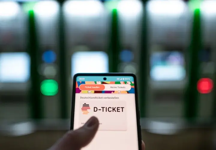 Smartphone zeigt "D-TICKET" an, bereit für das Deutschlandticket per Lastschrift. Im Hintergrund unscharfe Automaten.