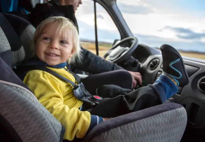 Glückliches Kind im Kindersitz im Bus. Die Füße des Kindes ragen über das Armaturenbrett.