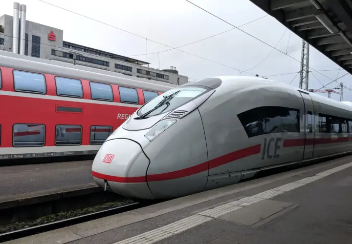 ICE-Zug und roter Regionalzug am Bahnsteig. Der ICE ist bereit für die Fahrt, wie ein ausgedrucktes Ticket zum Einsteigen.