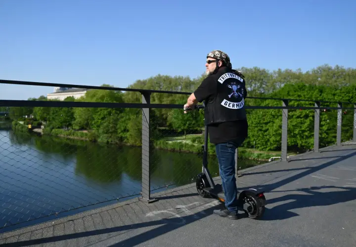 Mann mit Weste und Totenkopf-Bandana auf E-Scooter, genießt die Aussicht. Die Reichweite des E-Scooters ist für die Fahrt über die Brücke ausreichend.