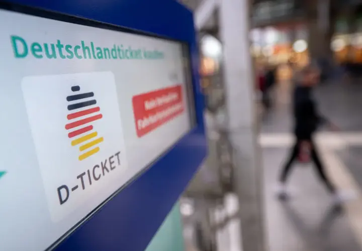 Das Deutschlandticket-Logo auf einem Bildschirm. Eine Person geht unscharf im Hintergrund vorbei. Vielleicht kann man das Deutschlandticket pausieren.