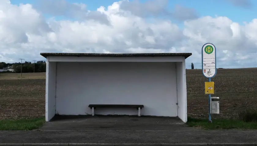 Ein Bushäuschen mit Bank und Haltestellenschild. Dieses Verkehrsmittel mit H-Symbol wartet auf Fahrgäste.