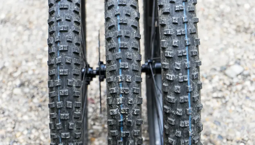 Drei breite Ballonreifen eines Mountainbikes mit grobem Profil und blauer Mittellinie. Bereit für jedes Gelände.
