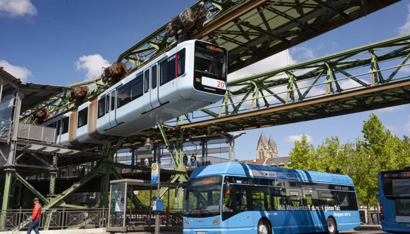 Die Schwebebahn Wuppertal fährt über einem blauen Bus. Mit dem Deutschlandticket ist das ganze Tal mobil.
