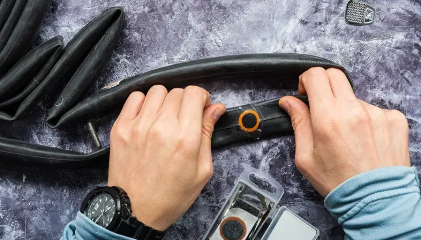 Hände reparieren einen Fahrradschlauch mit einem Flicken. Werkzeug und Flickzeug liegen bereit.