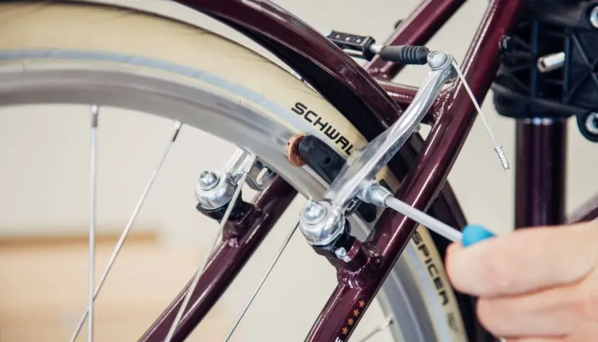 Hand wechselt Bremsbacken am Fahrrad mit Schraubendreher. Nahaufnahme des Bremsmechanismus am Rad.