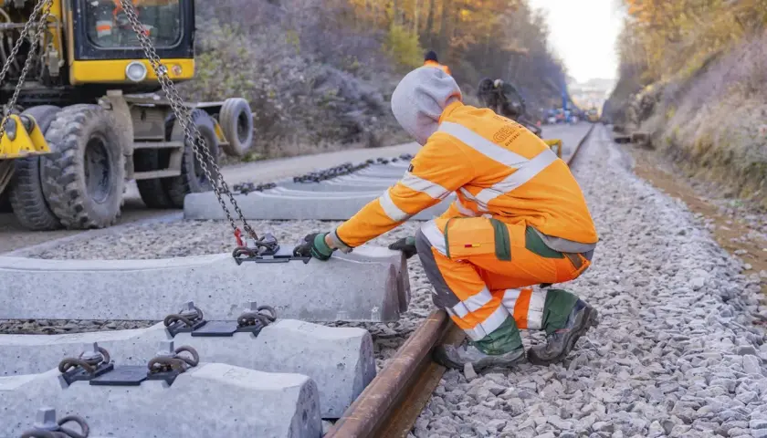 Arbeiter bei Bauarbeiten der Deutschen Bahn in NRW legen neue Betonschwellen. Ein Bagger hebt die schweren Teile an.